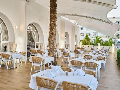 Světlá terasa s bílými prostřenými stoly a proutěnými židlemi v hotelové restauraci.