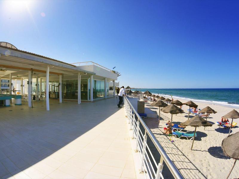 Grande terrasse avec sièges et vue sur la plage de sable ensoleillée et l'océan.