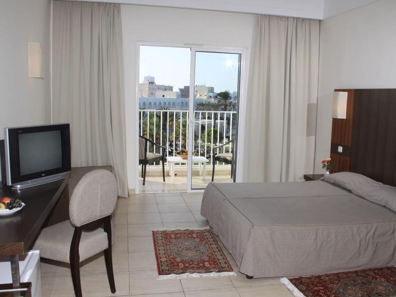 Chambre d'hôtel avec lit double, bureau avec chaise, balcon et vue sur la ville