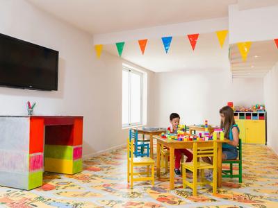 Bambini che giocano a un tavolo in una stanza luminosa e colorata con TV e decorazioni.