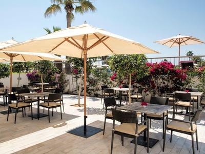 Terrazza esterna soleggiata con tavoli, sedie e grandi ombrelloni.