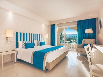 Camera d'hotel moderna con letto matrimoniale, accenti blu e balcone con vista sul mare.