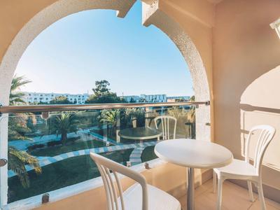 Balcone con tavolo e sedie con vista su piscina e edifici sotto cielo azzurro.