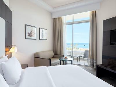 Helles Hotelzimmer mit großem Bett, Sofa, Balkon und Blick aufs Meer.