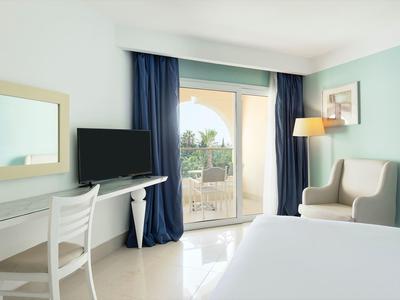 Camera d'hotel luminosa con letto, TV, scrivania e balcone con vista.