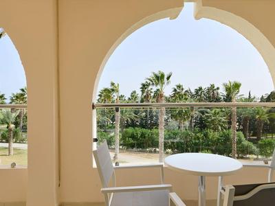 Terrazza con tavolo rotondo e sedie vicino a una ringhiera di vetro, palme sullo sfondo.