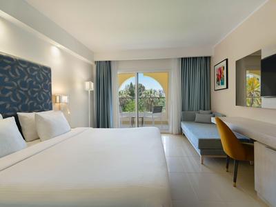 Modernes Hotelzimmer mit großem Bett, Schreibtisch und Blick auf die Terrasse.