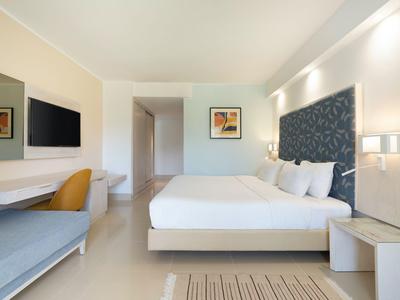 Modernes Hotelzimmer mit großem Bett, Fernseher und Sitzbereich in hellem Design.