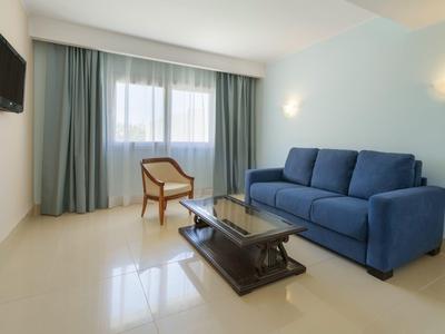 Modernes Hotellounge-Zimmer mit blauer Couch, Holztisch, Stuhl und Fernseher an der Wand.