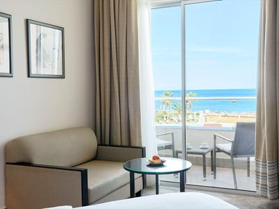 Hotelzimmer mit Badewanne und Balkon mit Meerblick bei klarem Himmel.