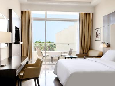 Helles Hotelzimmer mit großem Bett, Schreibtisch und Balkon mit Blick ins Grüne.