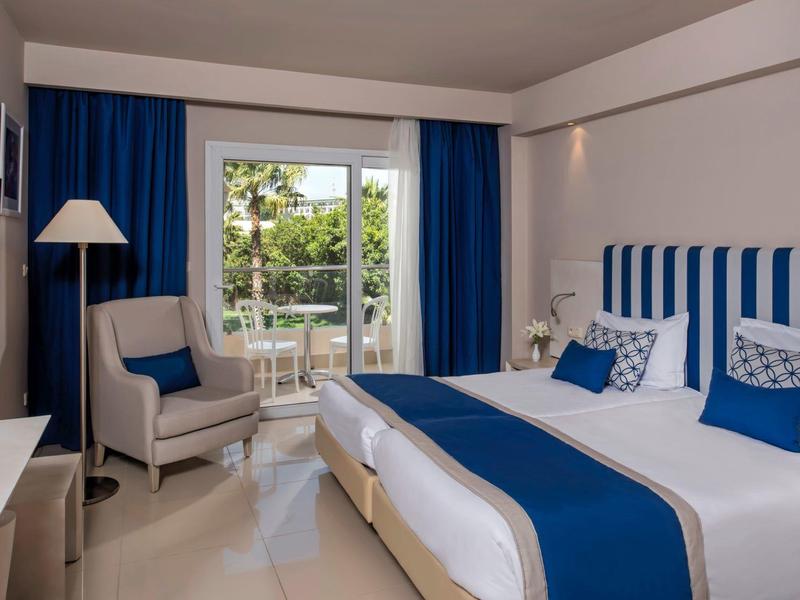 Camera d'hotel moderna con arredamento blu e vista su terrazza e giardino.