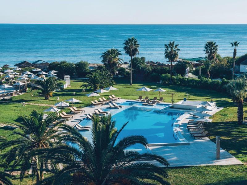 Piscina dell'hotel con lettini, palme e vista sul mare sullo sfondo.