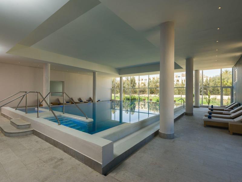 Area piscina interna moderna con lettini e grandi finestre con vista sul giardino.