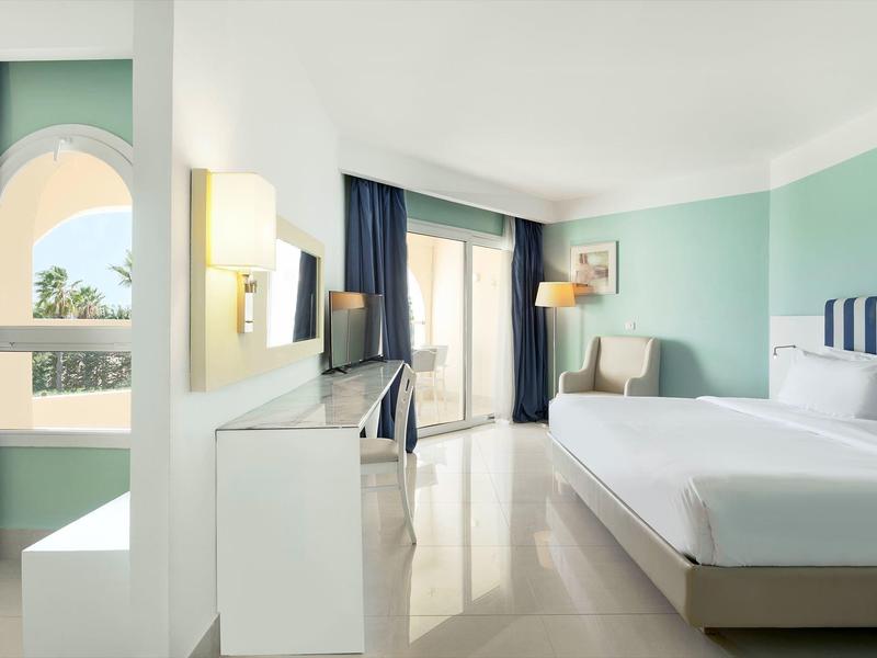 Camera d'hotel luminosa con letto grande e balcone con vista sul mare.