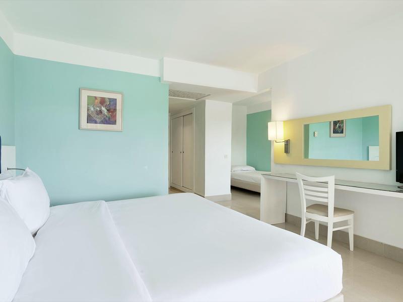 Camera d'hotel luminosa con letto matrimoniale, scrivania, sedia e TV a schermo piatto in colori tenui.