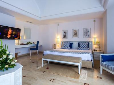 Chambre d'hôtel lumineuse avec lit double, coin salon et grandes fenêtres.