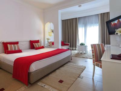 Chambre d'hôtel moderne avec grand lit, accents rouges et balcon.