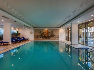 Espace intérieur avec grande piscine éclairée et chaises longues au bord.