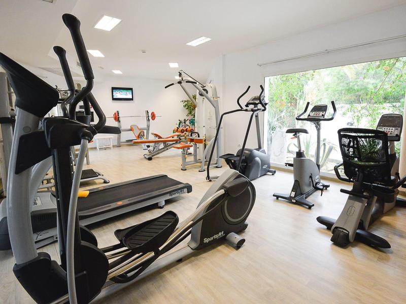 Salle de sport lumineuse avec des appareils de cardio et de grandes fenêtres donnant sur la verdure.