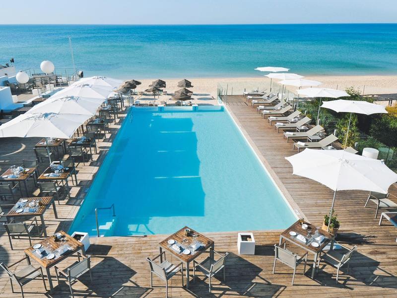 Piscine moderne avec transats et parasols au bord de la mer dans un complexe hôtelier.
