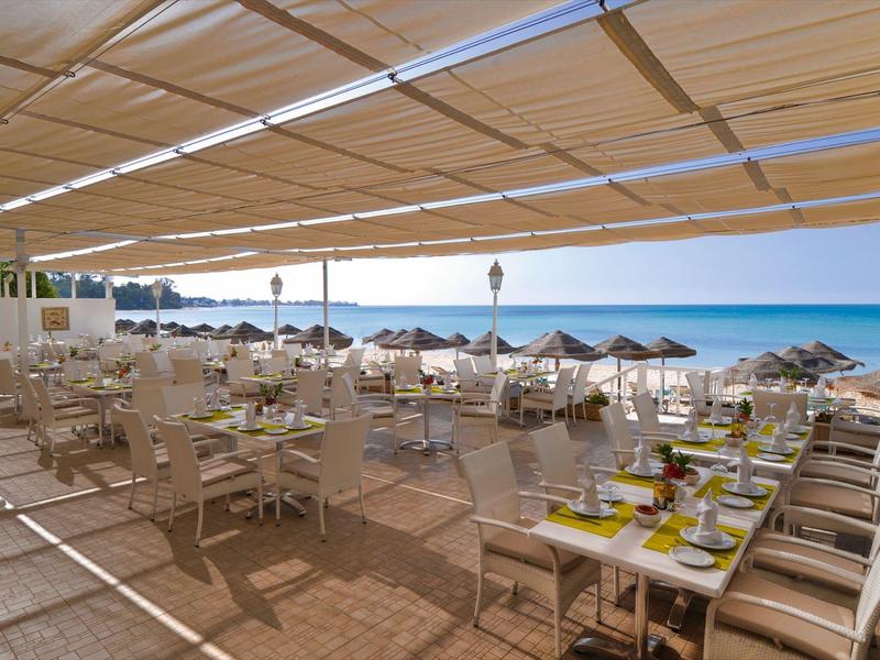 Terrasse ensoleillée avec tables dressées et vue sur la plage et la mer.