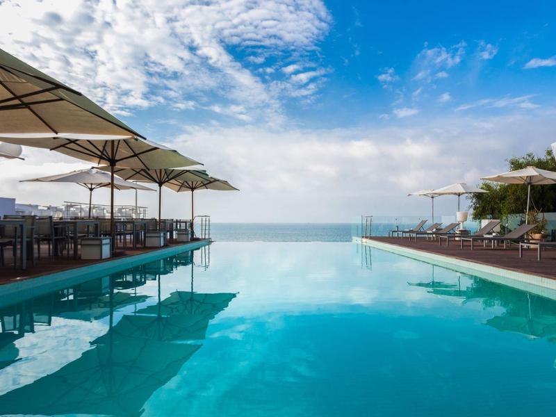 Piscine à débordement avec vue sur la mer, transats et parasols par une journée ensoleillée.
