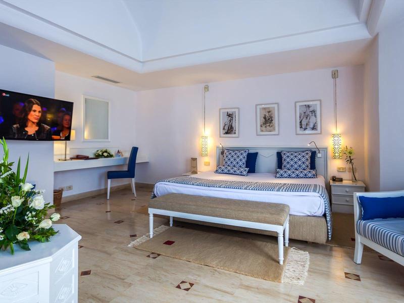 Chambre d'hôtel lumineuse avec lit double, coin salon et grandes fenêtres.