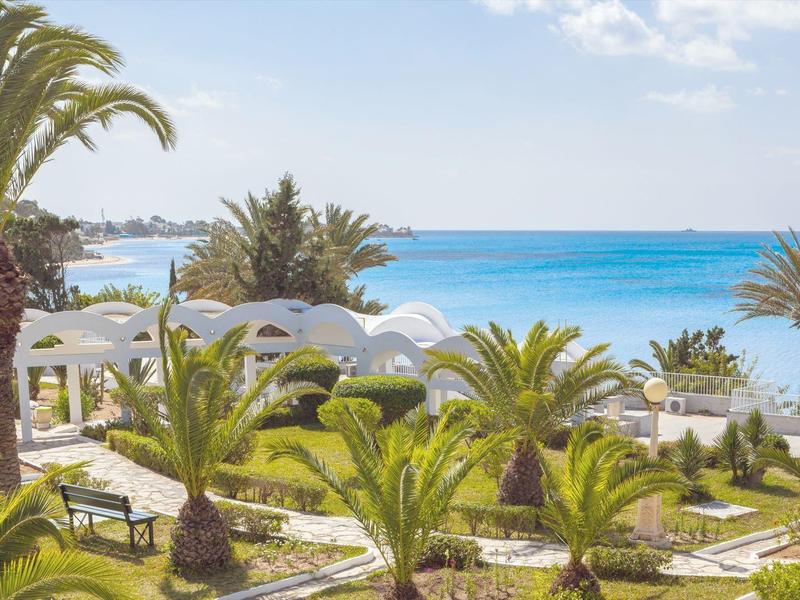 Station tropical avec des palmiers luxuriants près d'une mer bleu clair sous un ciel dégagé.