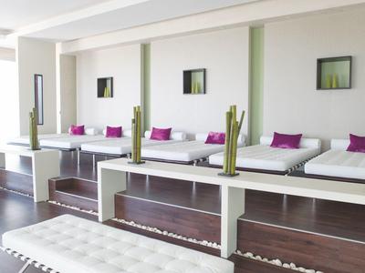 Heller Ruheraum mit niedrigen weißen Liegen, violetten Kissen und grünen Bambusdekorationen.