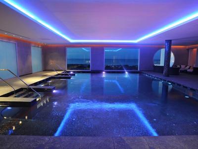 Innenpool mit LED-Beleuchtung, Liegestühlen und großer Fensterfront zur Aussicht.