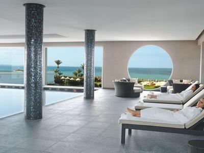 Modernes Hotel mit Pool, Sonnenterrasse und Meerblick durch großes Rundfenster.