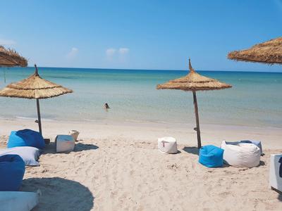 Strand mit Sand, zwei Sonnenschirmen und blauen sowie weißen Sitzkissen am Meer