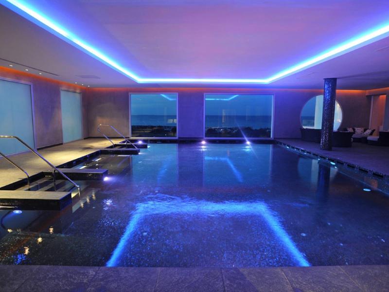 Innenpool mit LED-Beleuchtung, Liegestühlen und großer Fensterfront zur Aussicht.