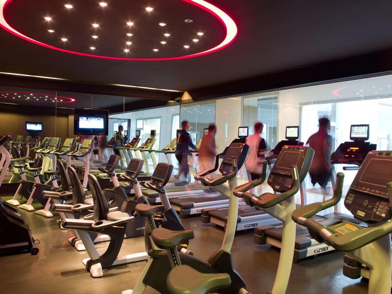 Moderne Fitnessstudio mit mehreren Laufbändern, elliptischen Maschinen und großem Fenster.