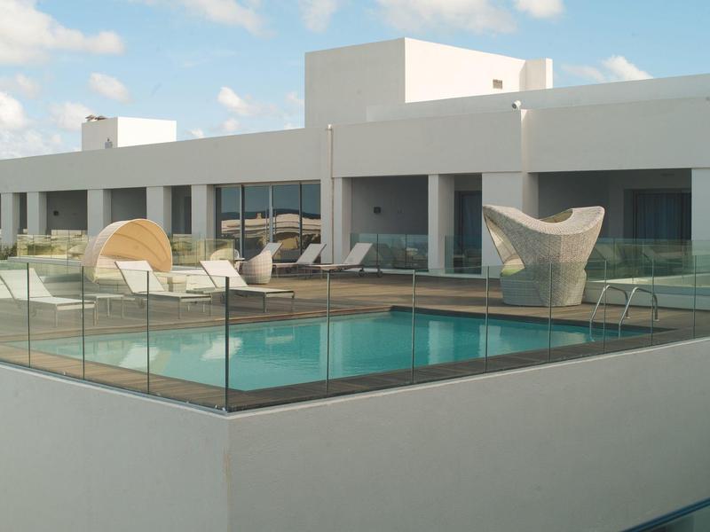 Moderner Poolbereich vor einem weißen Haus mit Glasabgrenzung und Sonnenschirm.