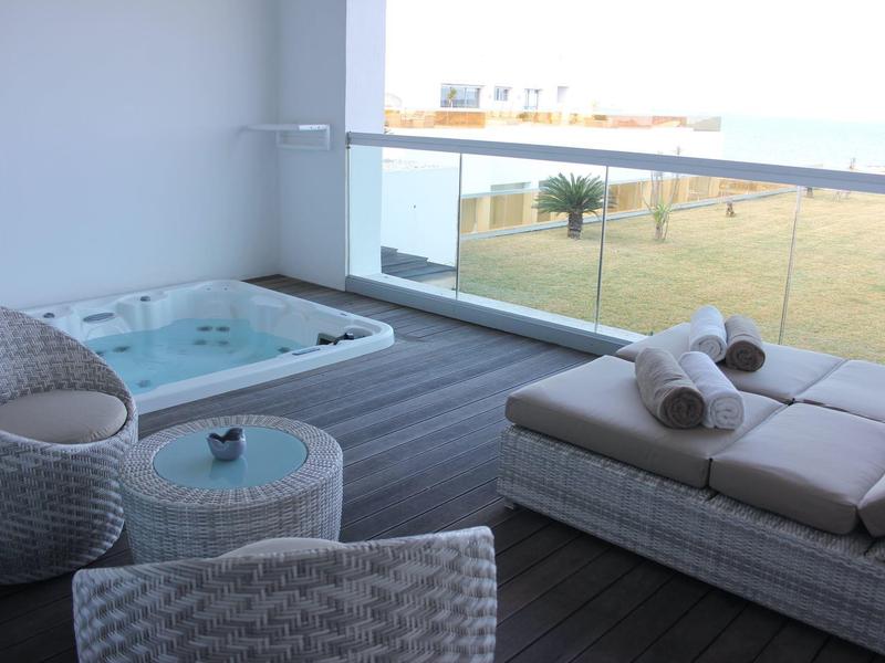 Moderne Terrasse mit Whirlpool, Sonneliege und Stühlen, Blick auf Rasen und Glasgeländer.