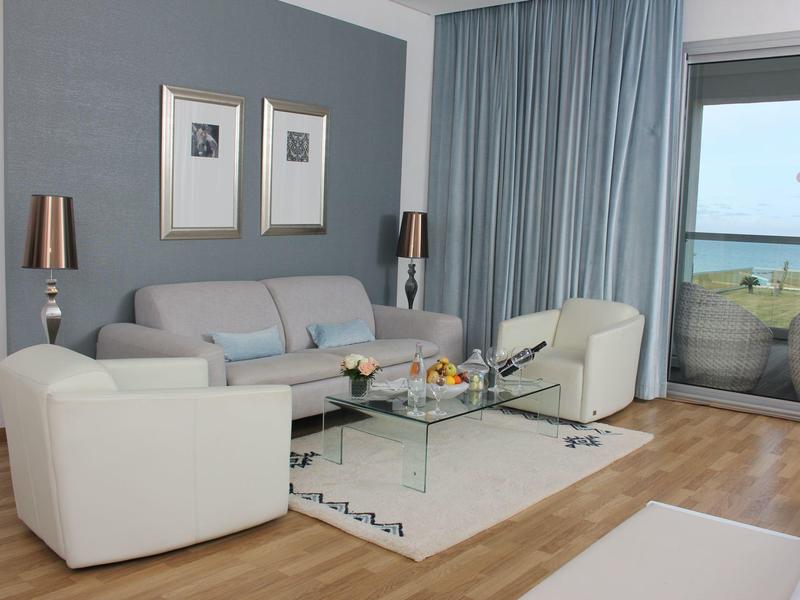 Modernes Wohnzimmer mit Sitzecke, Glas-Couchtisch und Meerblick durch Panoramafenster.