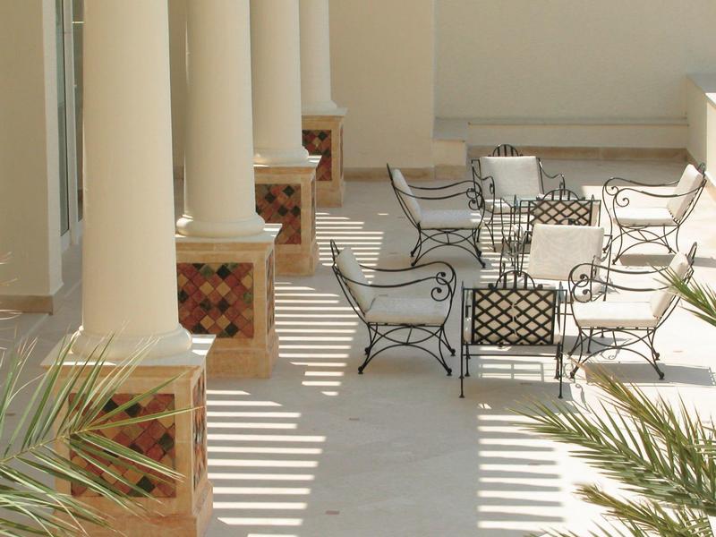 Terrasse mit Säulen, Metallstühlen und Tischen in hellem, sonnendurchflutetem Raum.