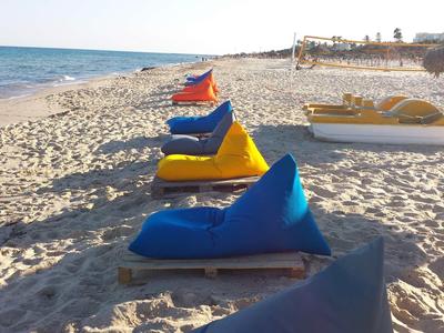 Mehrere bunte Sitzsäcke auf einem Sandstrand mit Blick auf das Meer.