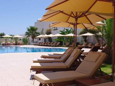 Bequeme Liegestühle unter Sonnenschirmen neben einem klaren Pool in einem Hotelgarten.