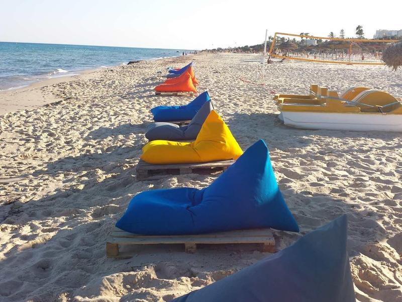 Několik barevných lehátek na písečné pláži s výhledem na moře při západu slunce.