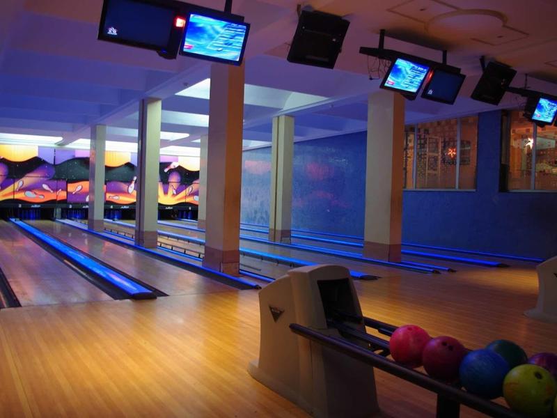 Moderní bowlingová dráha s několika dráhami, barevnými koulemi a obrazovkami pro zobrazení skóre.