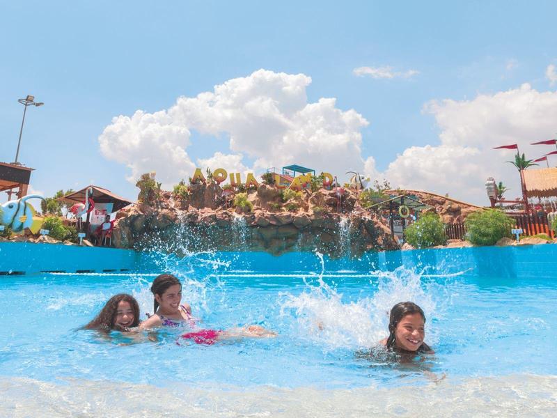 Bambini che si divertono in una grande piscina di parco acquatico con rocce artificiali e scivoli.