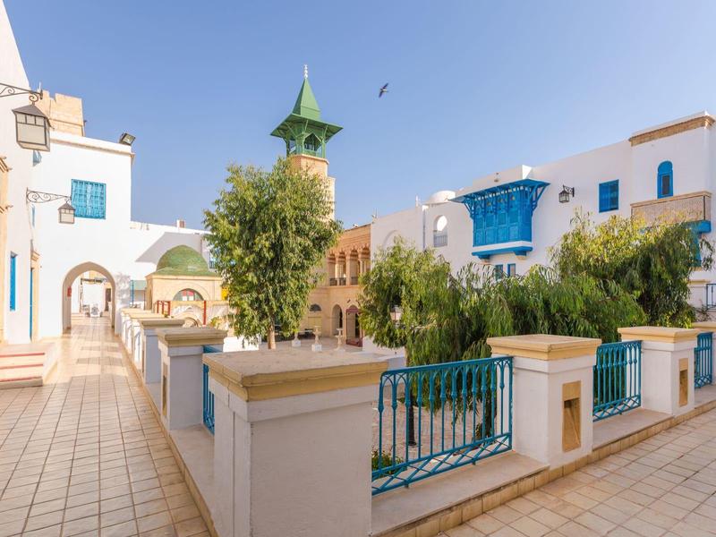 Cortile soleggiato con edifici bianchi e accenti blu in un villaggio in stile mediterraneo.