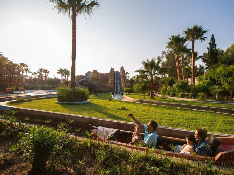Bambini giocano in un piccolo canale d'acqua circondato da palme e vegetazione sotto un cielo limpido.