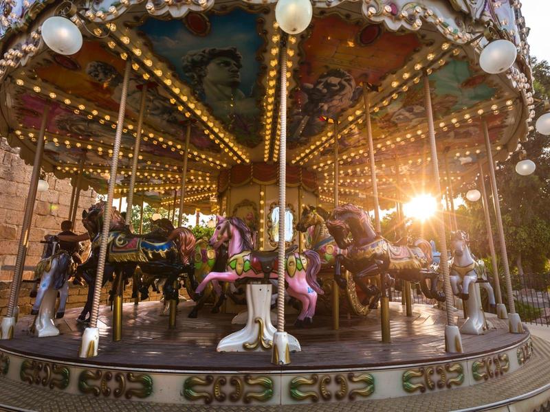 Una giostra illuminata con cavalli viola e bianchi all'aperto al tramonto.