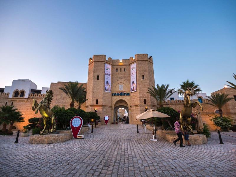 Fortezza storica in pietra con grande arco d'ingresso e palme sotto un cielo azzurro.