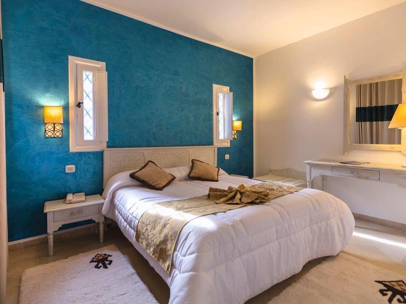 Camera d'hotel accogliente con letto matrimoniale, parete accentuata turchese, comodini e illuminazione soffusa.