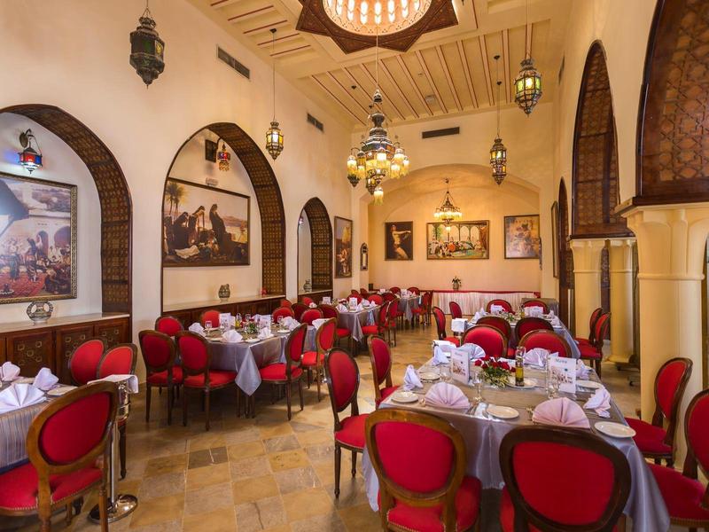 Sala da pranzo elegante dell'hotel con sedie rosse, tavoli rotondi e finestre ad arco.